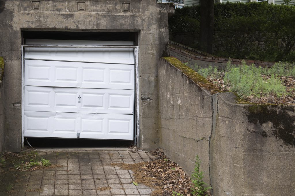 a white garage door that has many dents and it beat up. 