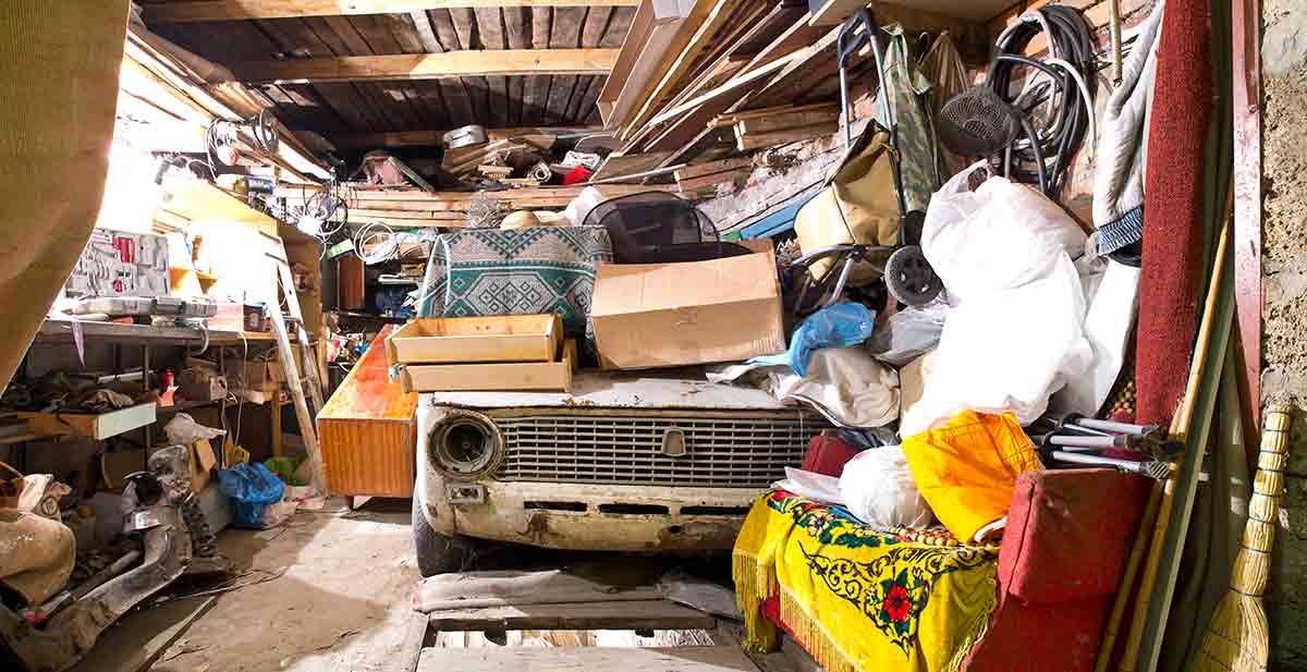 a dirty, cluttered garage with an old beat up car in it