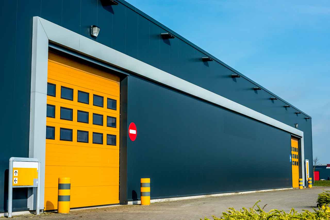 Modern yellow custom garage door with glass panels on a grey commercial building.